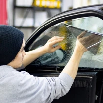Technician in a beanie installing window tint film on a partially wet car window