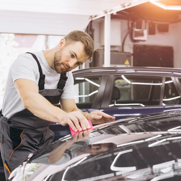 Technician applying product to the roof of a black car using a red applicator pad inside a detailing garage
