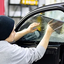 Technician in a beanie installing tint film on a partially sprayed car window