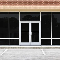 Commercial glass storefront with black window tint and a double-door entrance beneath a red brick wall