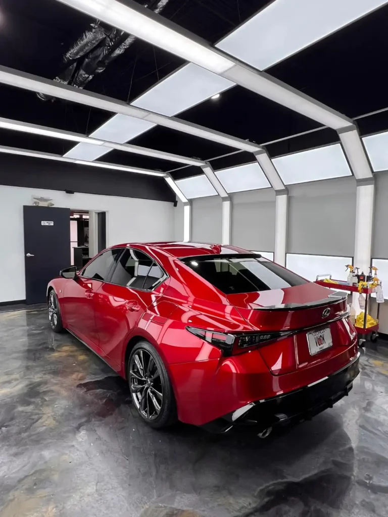 Shiny red Lexus sedan inside a detailing studio with white panel lighting and a clean, glossy floor