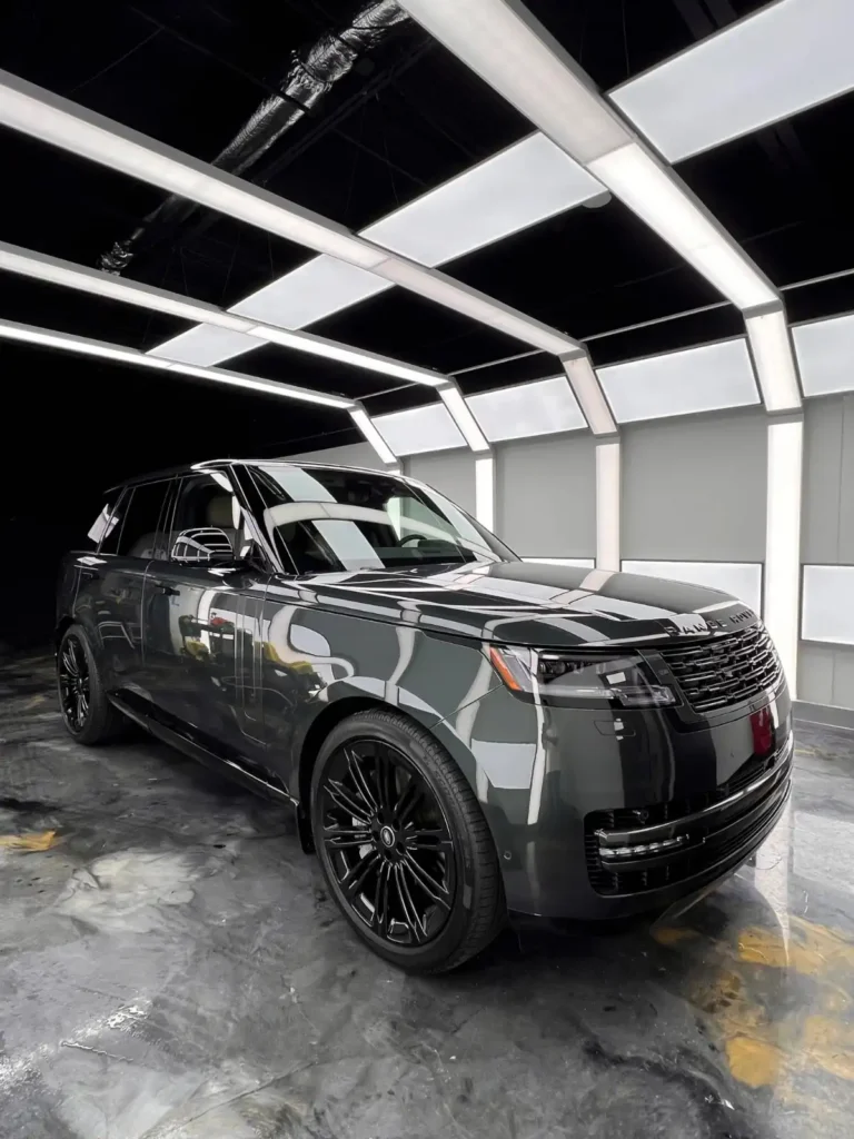 Glossy black Range Rover SUV parked inside a modern detailing studio with white overhead lights and a polished floor