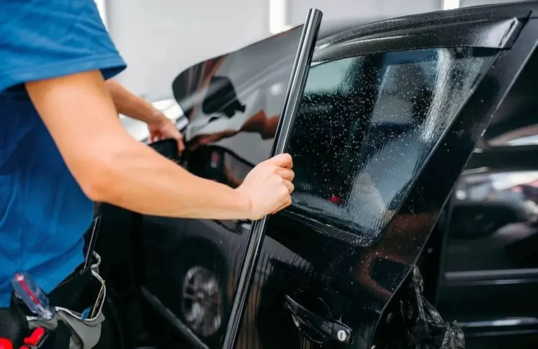 Close-up of a technician applying wet tint film to a black car window using a smoothing tool