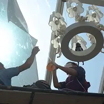 Two workers installing window film on a large skylight or ceiling window with sunlight streaming in