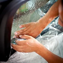 Close-up of hands applying clear film to a car window during tinting or paint protection process