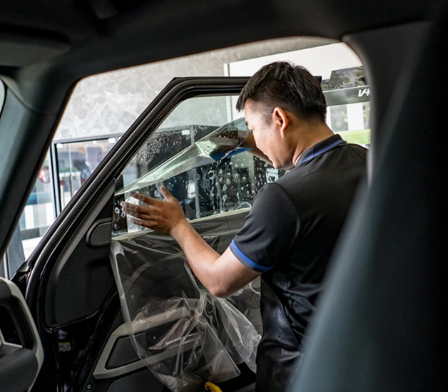 Technician carefully applying a transparent film to the driver-side window of a black SUV
