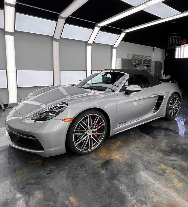 Silver Porsche 718 Boxster GTS 4.0 convertible inside a high-end auto detailing bay with glossy floors and overhead lights